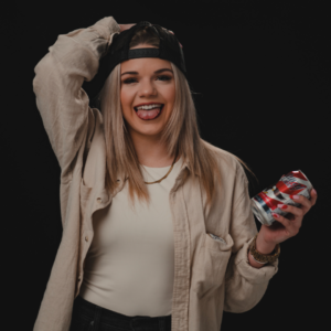 Chloe Pigue with her tongue out, backwards hat, and holding a can of beer