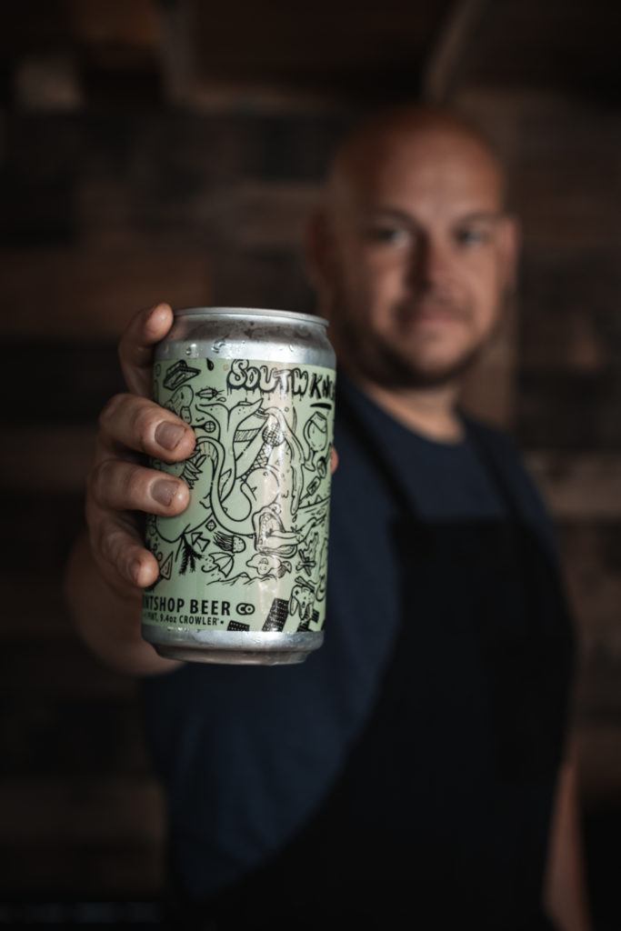 Product photography of a man holding out a can of Printshop Beer.