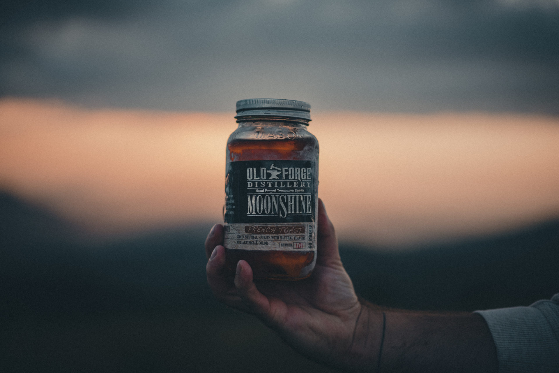 Product photography of a man holding a frosty bottle of Old Forge Distillery moonshine.