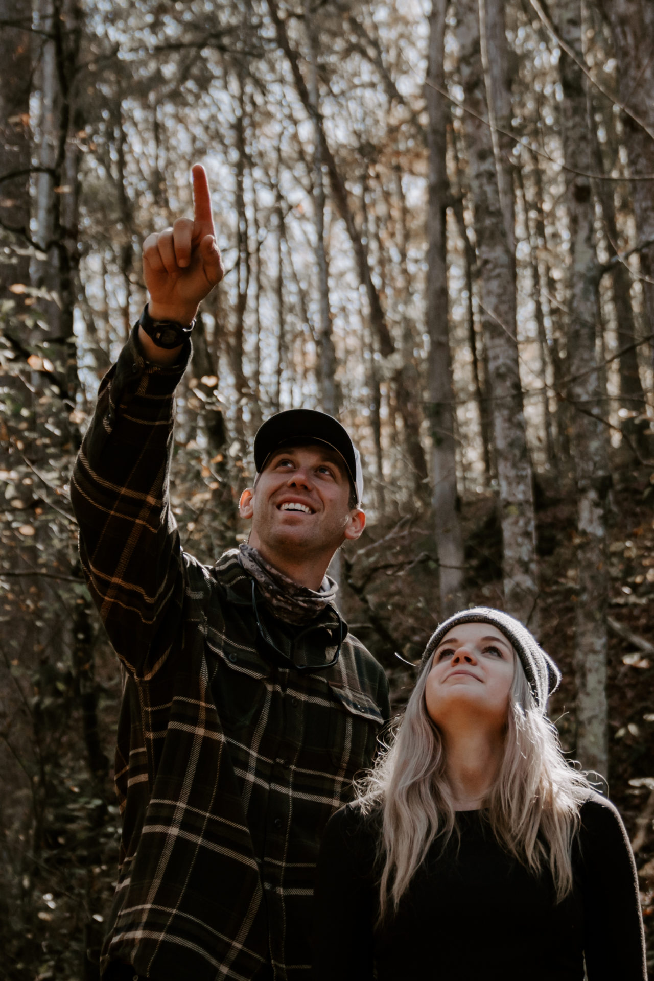 Lifestyle photography of a man and woman standing together in a wooded area and the man is pointing up at something.