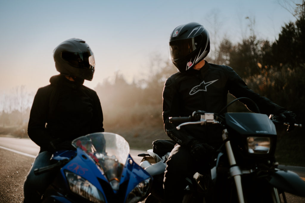 Lifestyle photography of two motorcyclists looking at each other while sitting on their bikes.