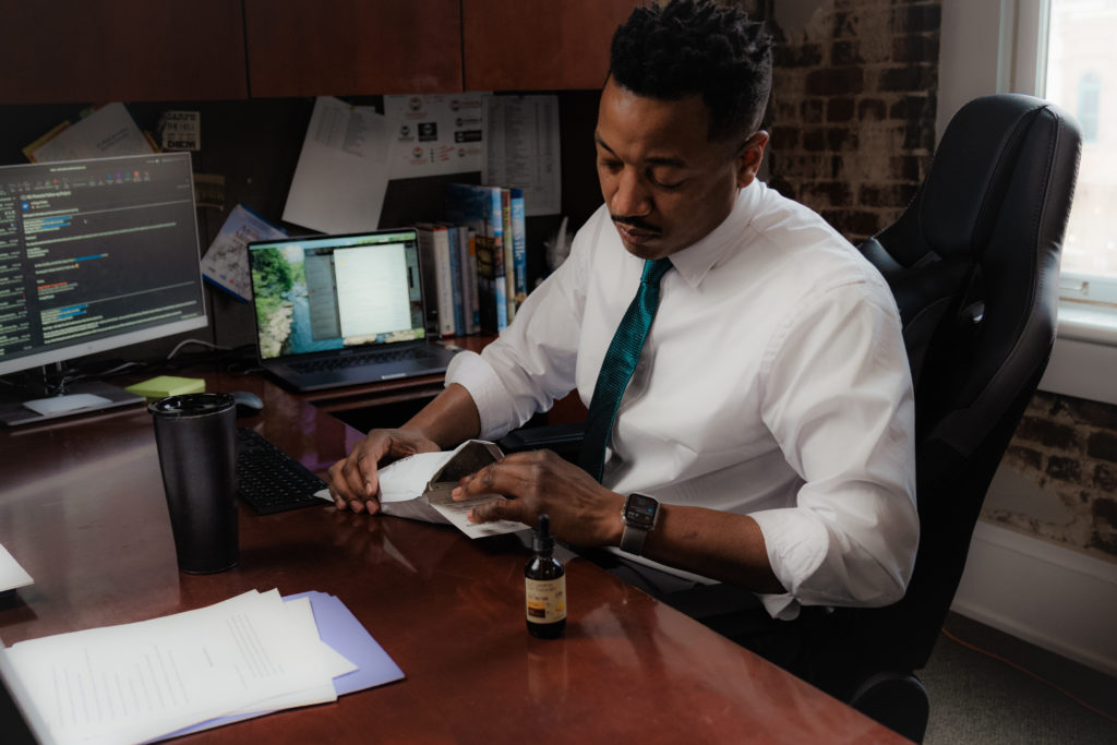 Product photography of a man sitting at his desk opening a package including CBD drops.