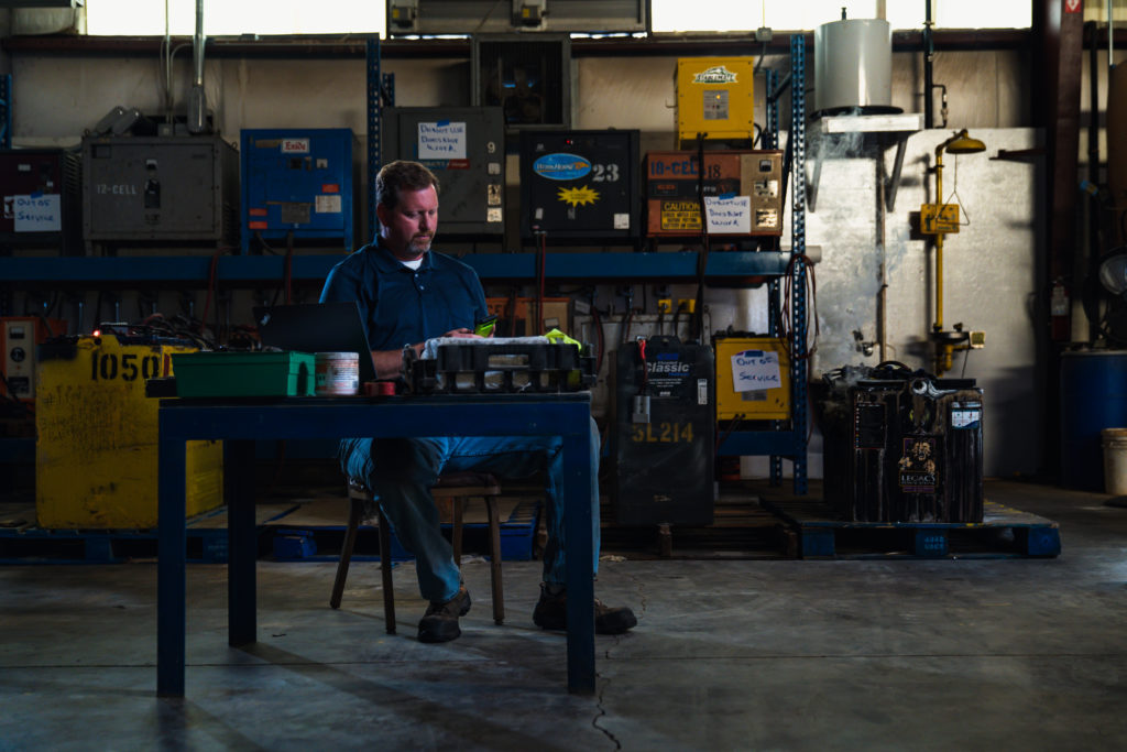 Commercial photography of a battery maintenance man sitting at his desk in front of a messy work station.