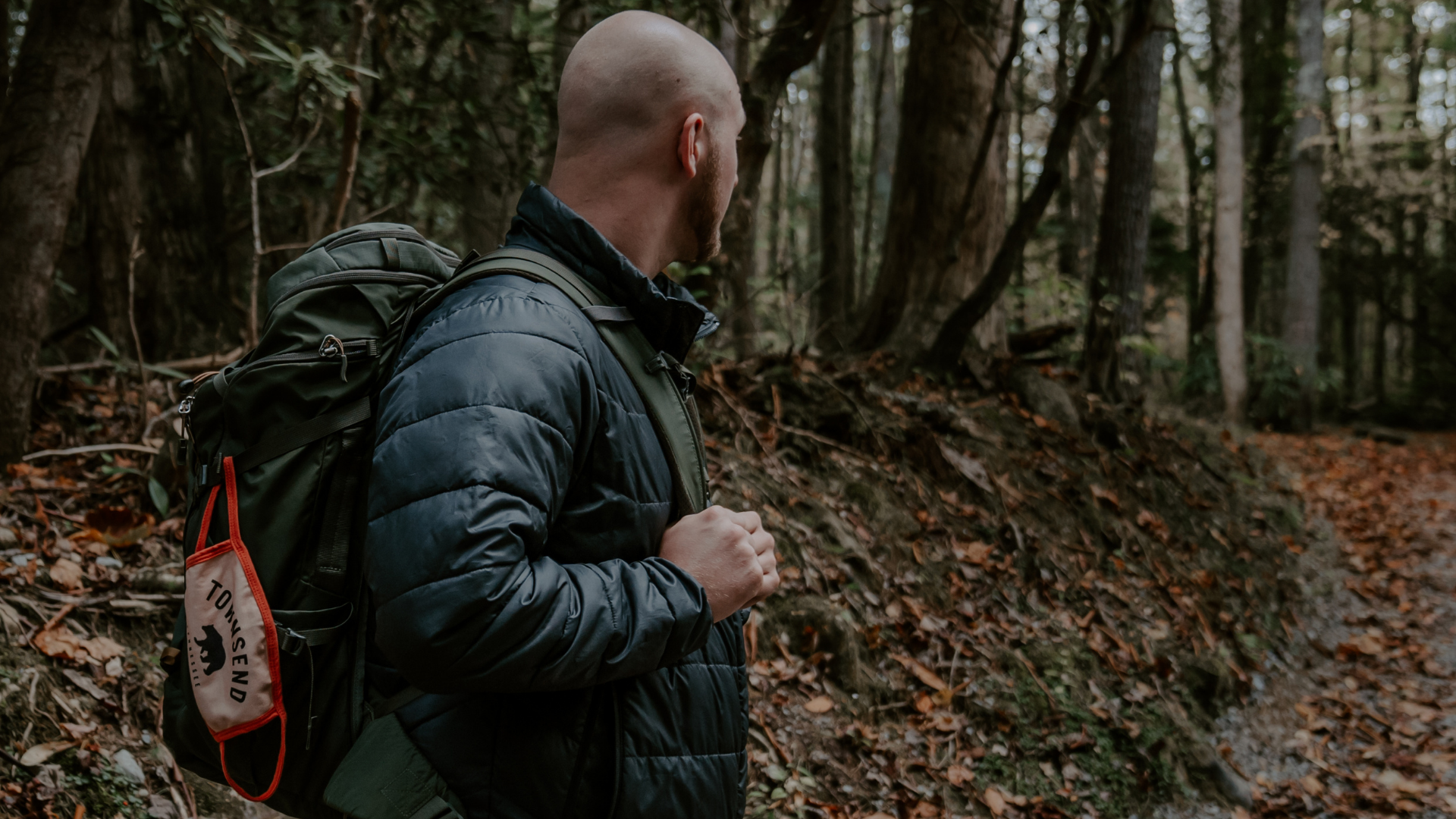 A man hiking in the Smoky Mountains with a Townsend mask on his backpack