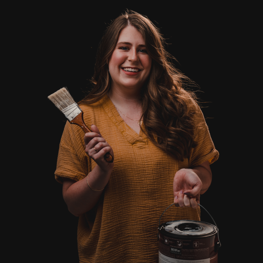 Megan Allen holding a paint brush and paint can smiling at the camera