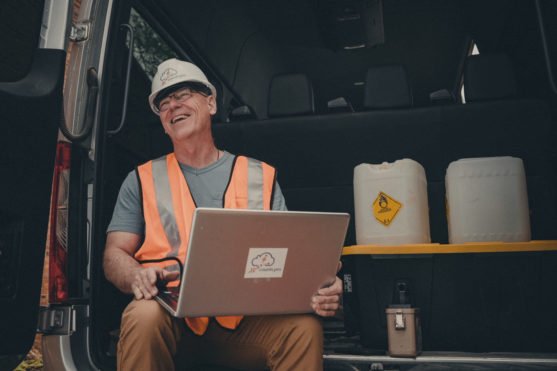 Commercial photography of an employee in an orange vest laughing while using a laptop.