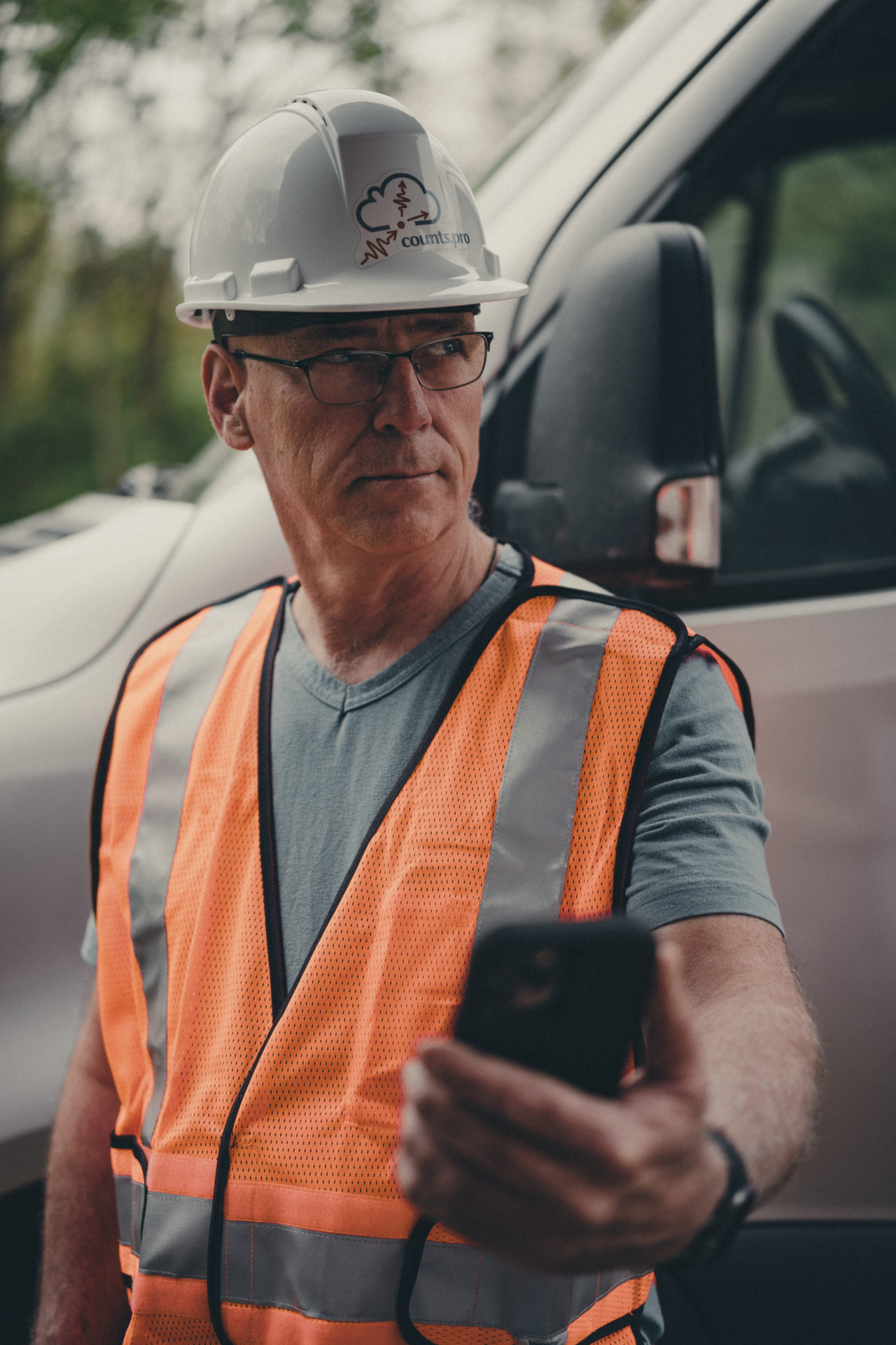 Commercial photography of an employee in an orange vest looking in the distance while holding a phone.
