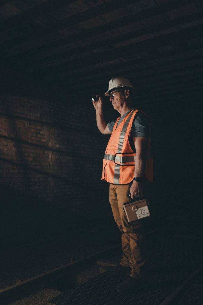 Commercial Photography of an employee in an orange vest using a flashlight to look into the dark.
