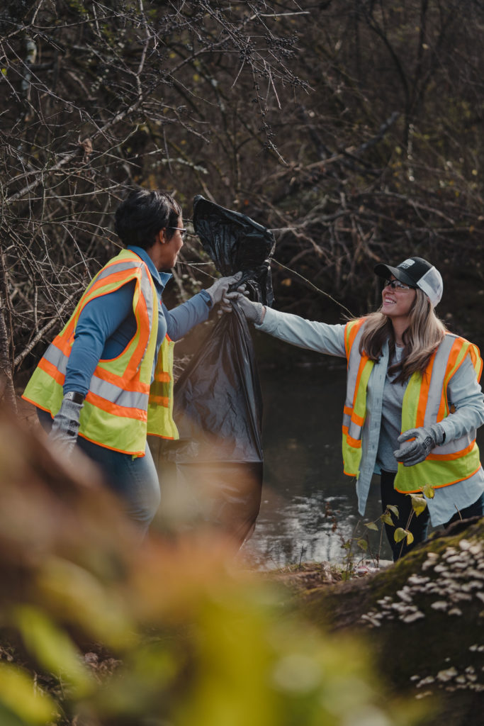 Lifestyle photography of two KUB employees picking up litter in a Knoxville Forest and smiling.