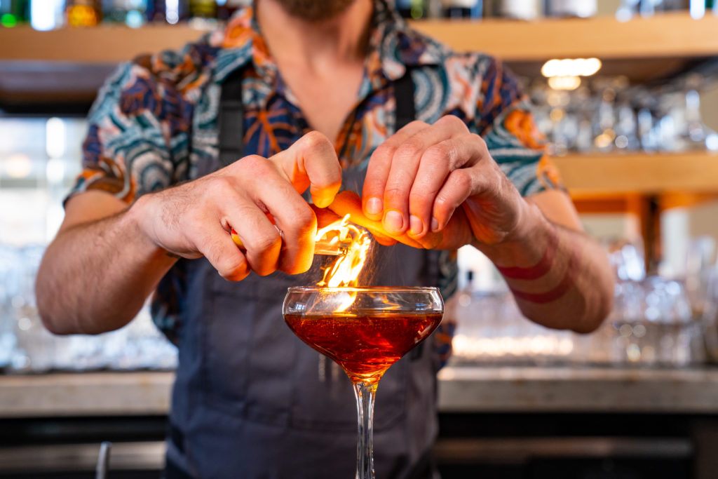 Close-up product photography of a bartender lighting a flame above a cocktail at Marble City Market in Knoxville, TN.