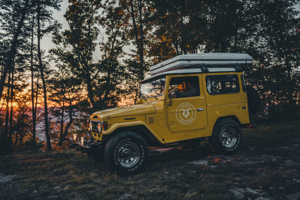 Commercial photography of a yellow classic Land Cruiser with a rooftop tent in front of a sunset in Chattanooga, TN.