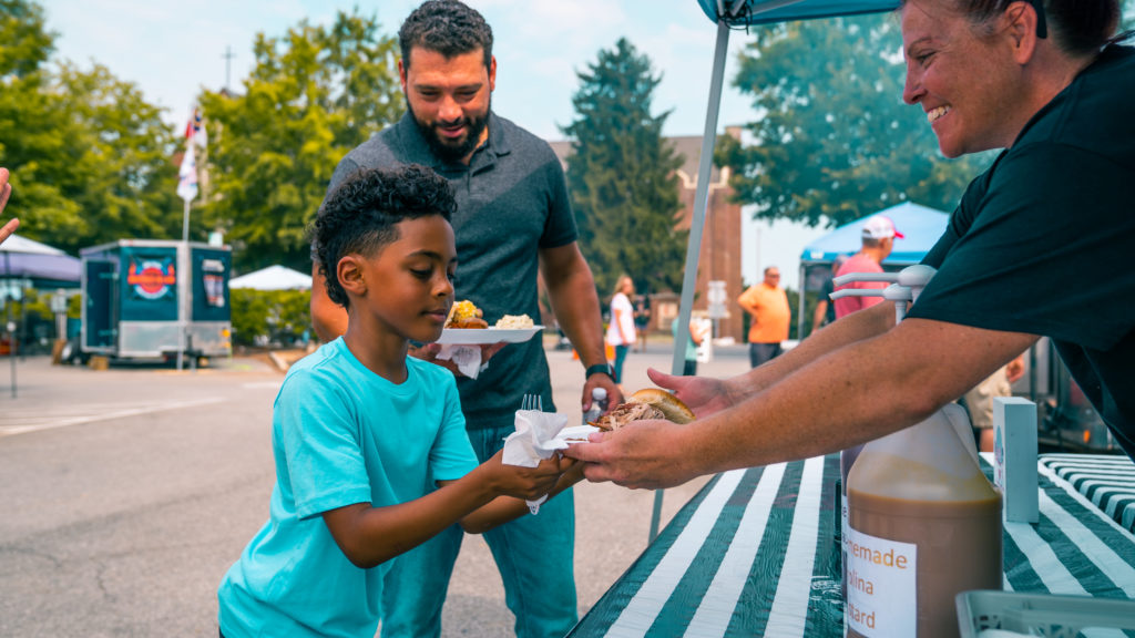 Event photography of a little boy getting food from a vendor while his dad stands in the background in Maryville, TN.
