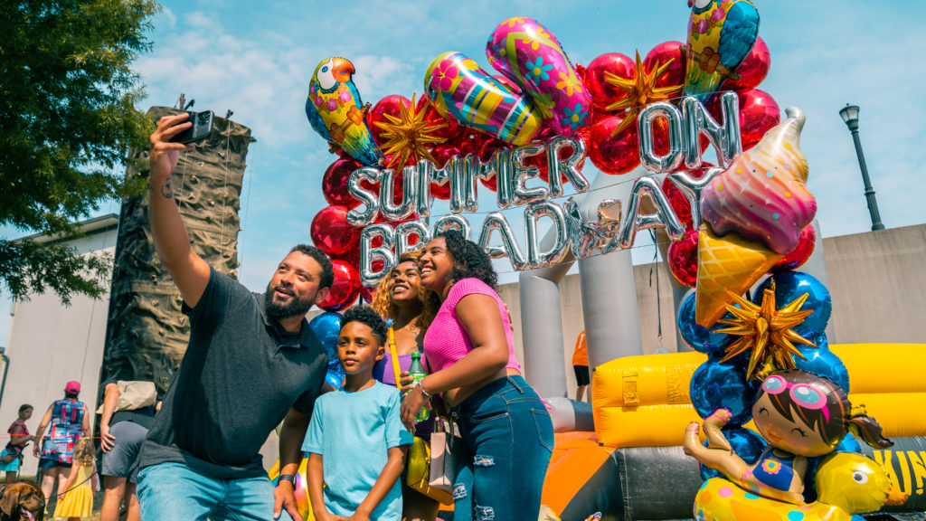 Event photography of a family taking a selfie in front of a Summer on Broadway balloon display in Maryville, TN.