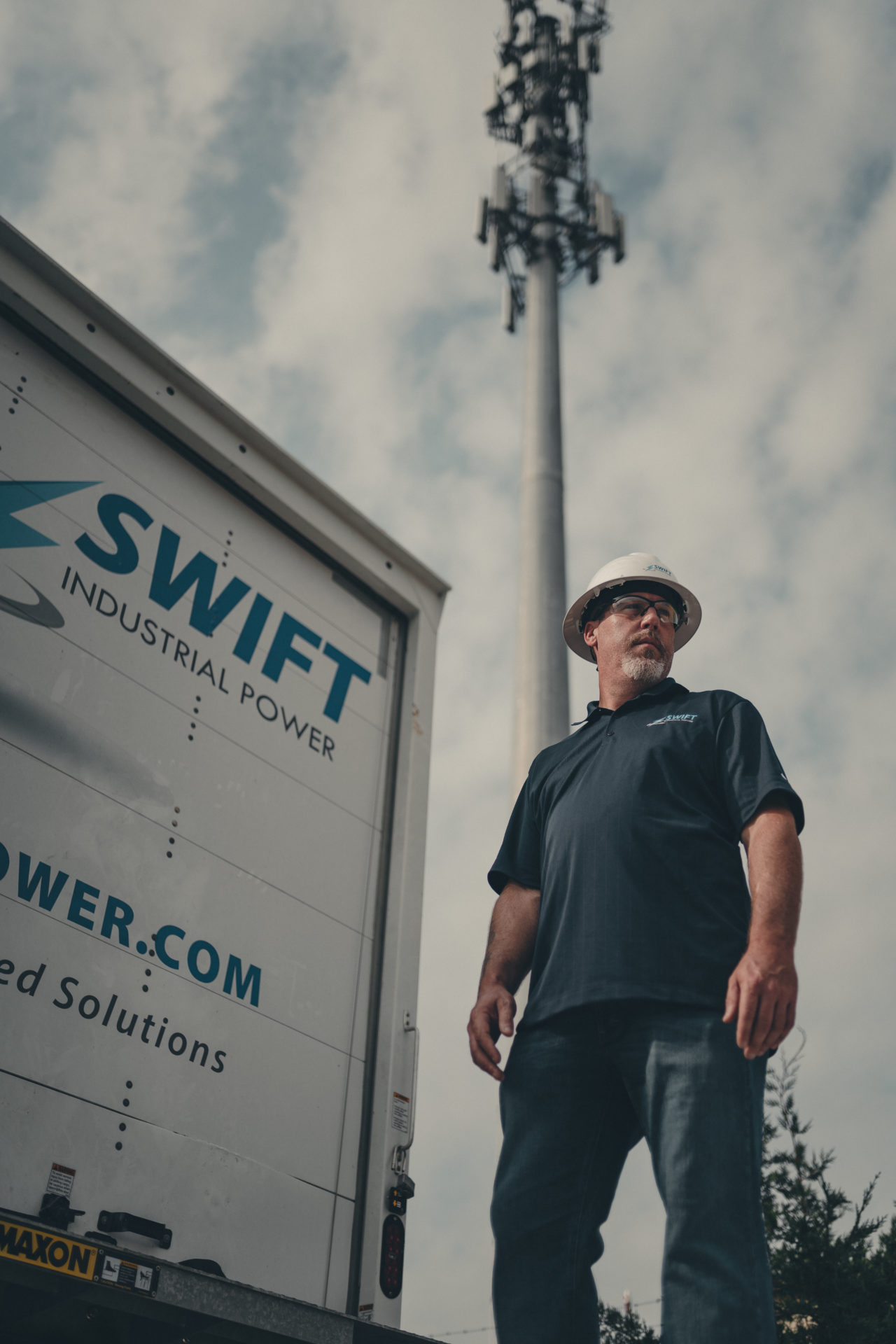 Commercial photography of a Swift Industrial Power employee standing with a cell site looming in the background.