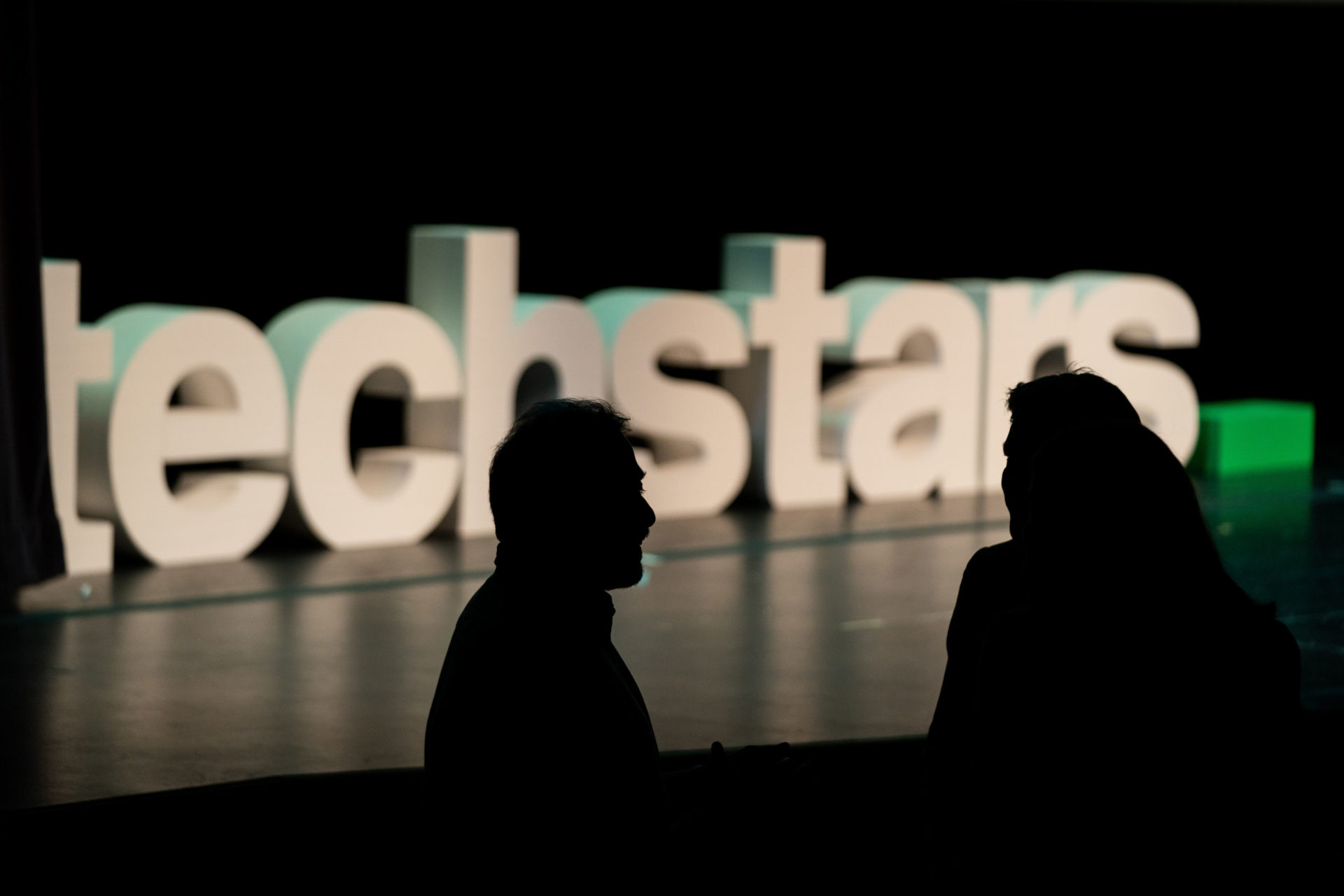 Event photography showing the outline of people with the techstars logo in the background.