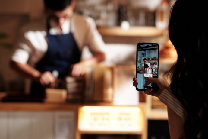 A person holding up a phone taking a video of someone working in a coffee shop