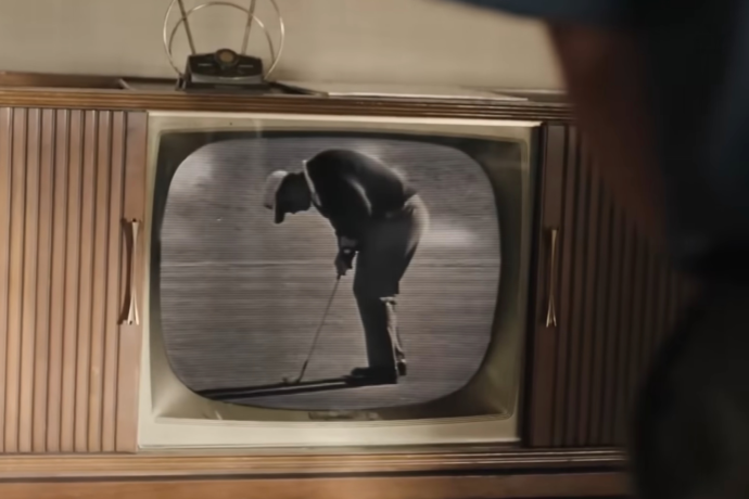 A vintage wooden television displays black-and-white footage of a golfer putting on a green, with part of a person visible in the foreground watching the screen.
