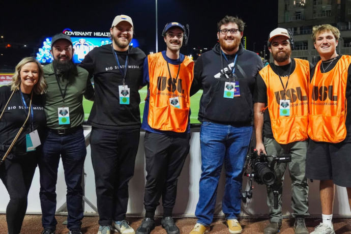 Big Slate Media production crew poses together on the sidelines of a soccer field at night, wearing event credentials and production gear after a One Knoxville SC match.