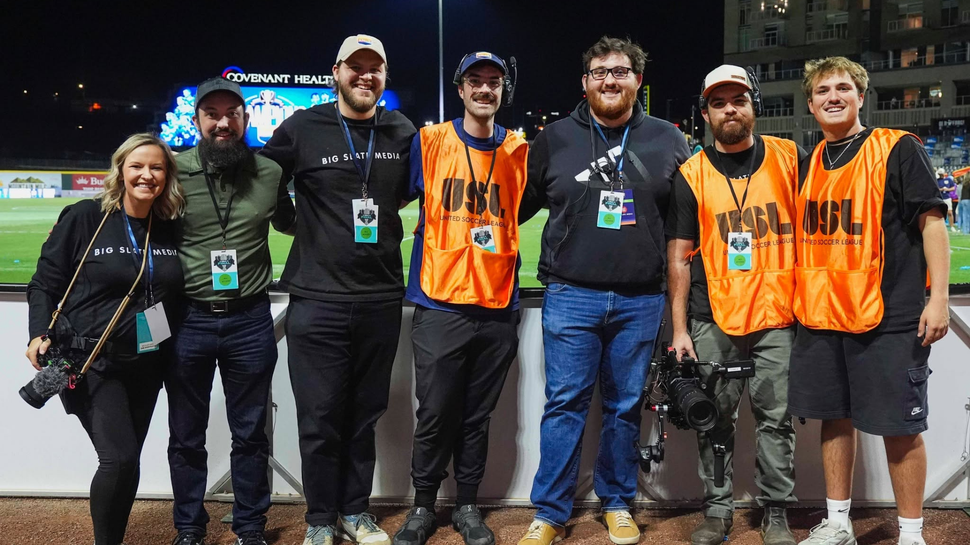 BSMxOneKnox Big Slate Media production crew poses together on the sidelines of a soccer field at night, wearing event credentials and production gear after a One Knoxville SC match.